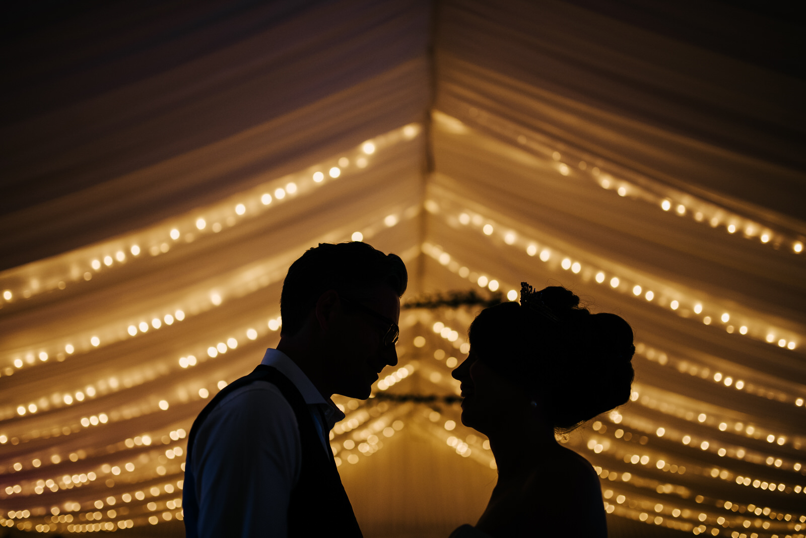 Silhouette portrait of bride and groom against marquee fairyligh