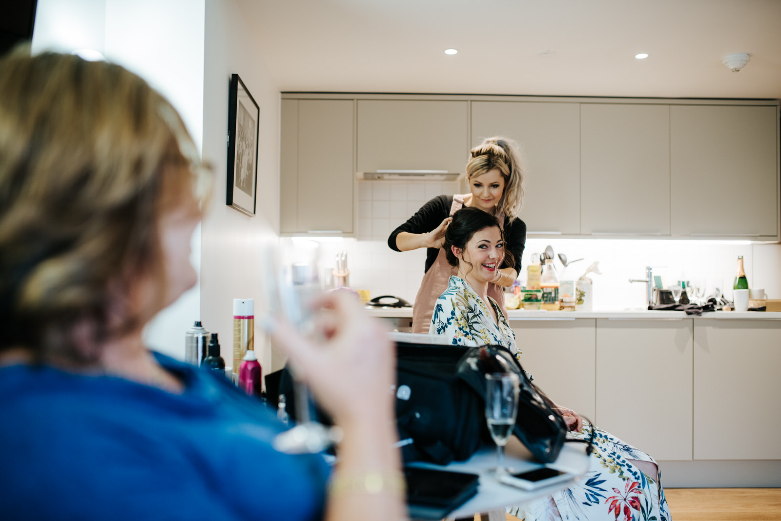 Bride getting her hair done while laughing and looking at mother