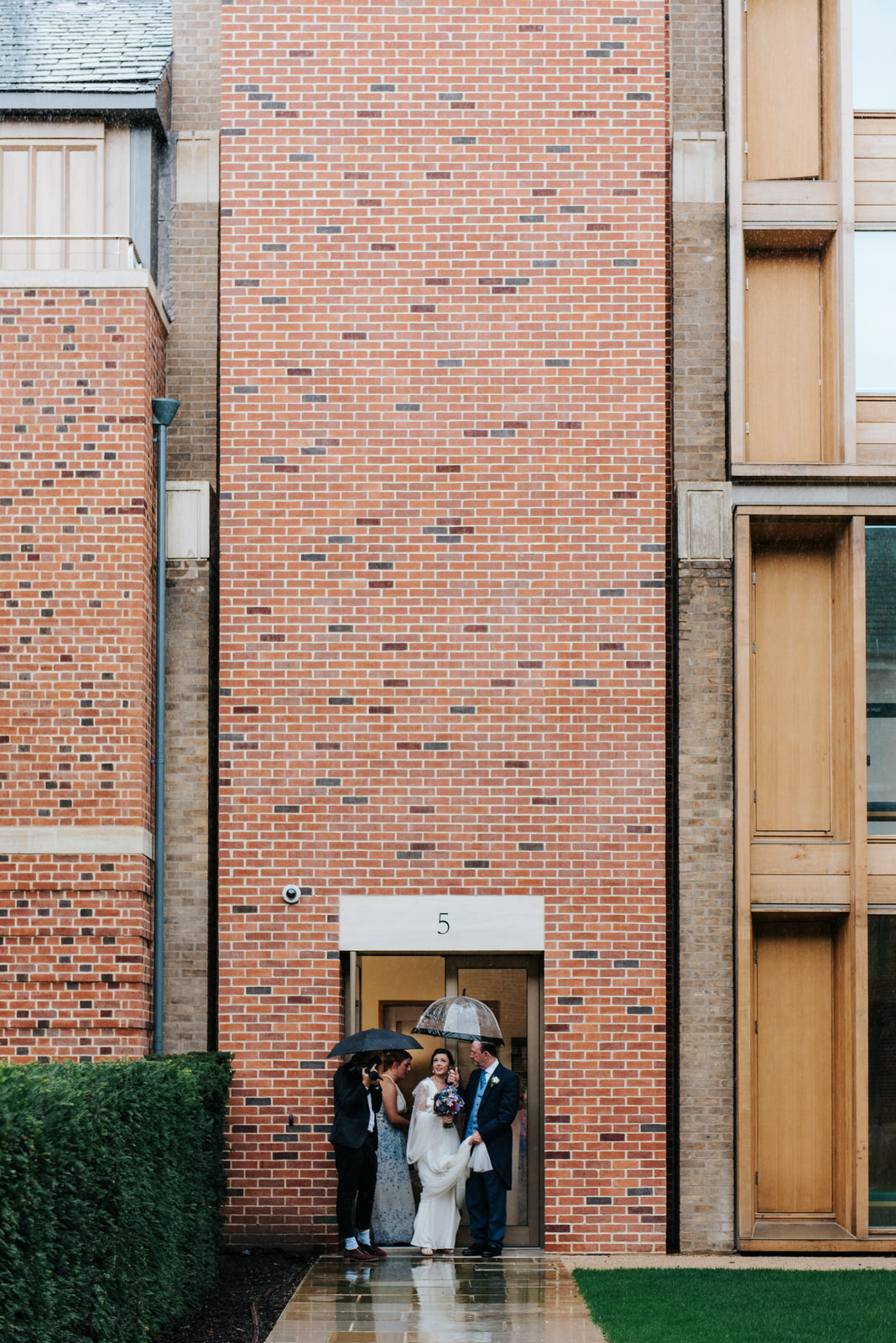 Bridal party leaves Jesus College accommodation under umbrellas 