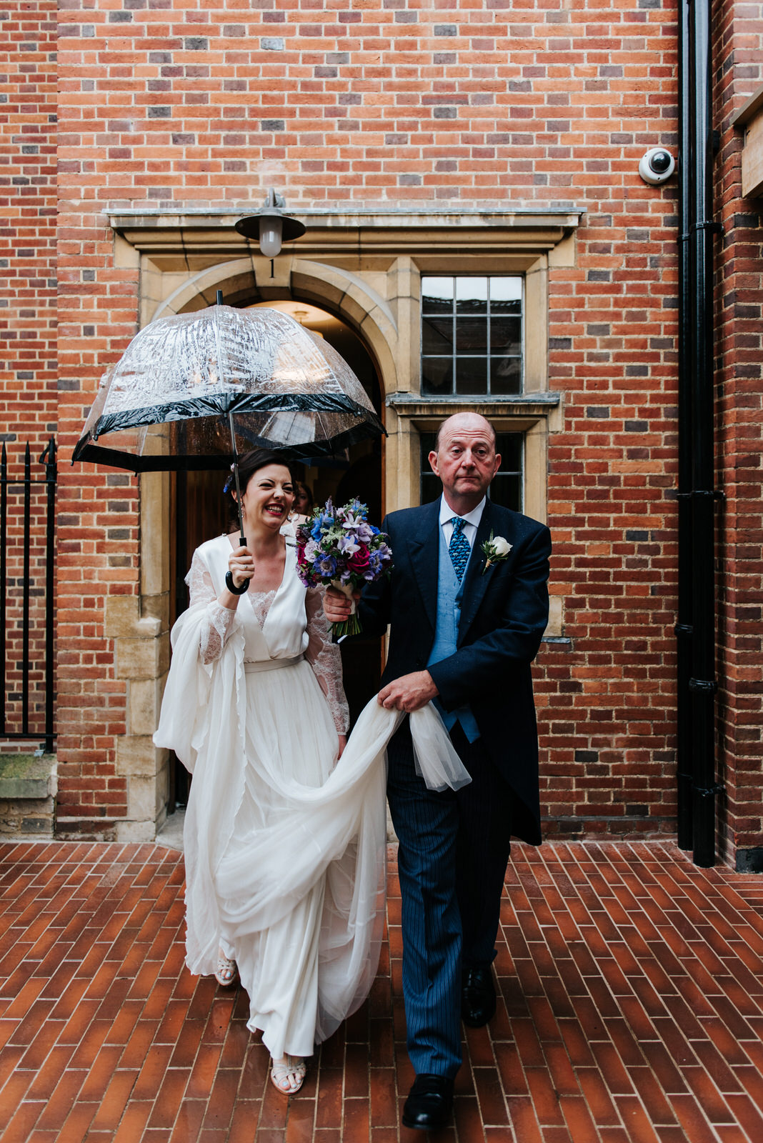 Bride and her father walk towards Jesus College chapel in the po