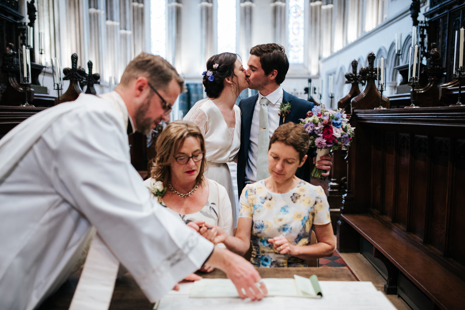 Bride and groom steal a kiss as witnesses sign register during w