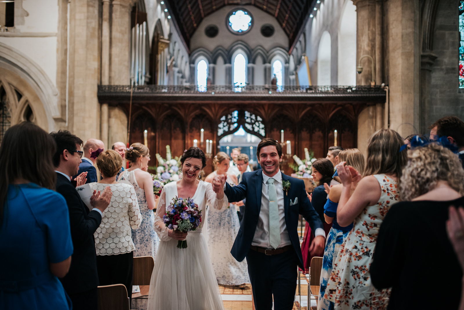 Bride and groom exit joyfully down the aisle at Jesus College Ca