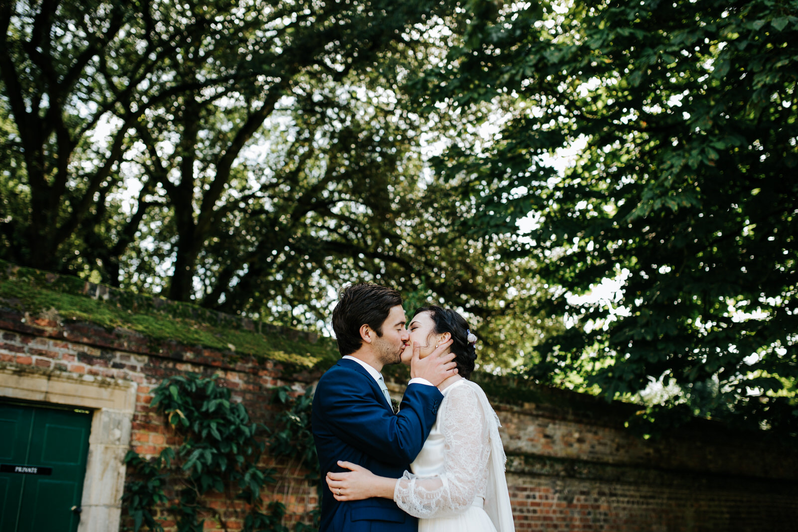 Bride and groom kiss under beautiful green trees during couple p