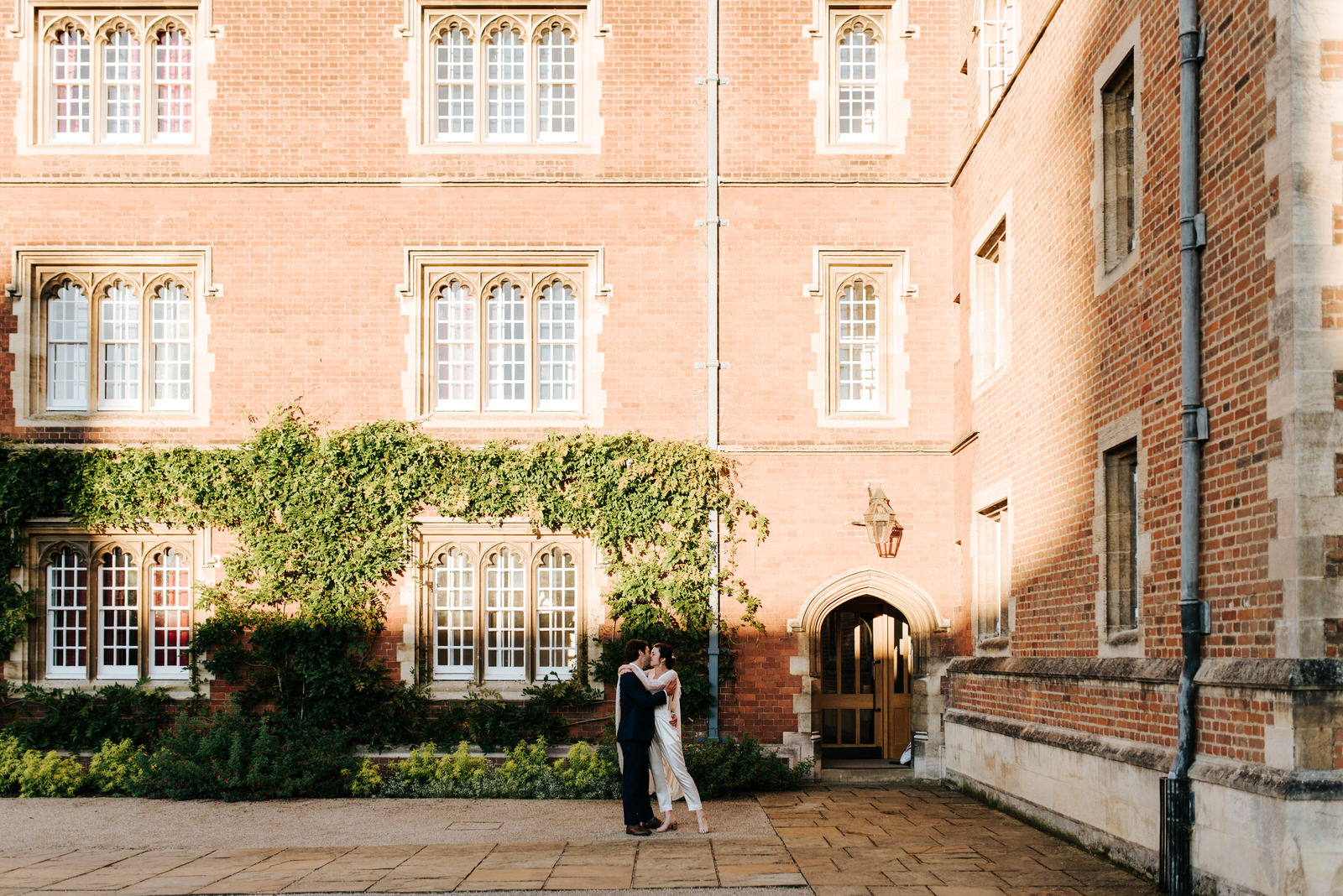 Bride and groom kiss and embrace in Jesus College Chapel Court