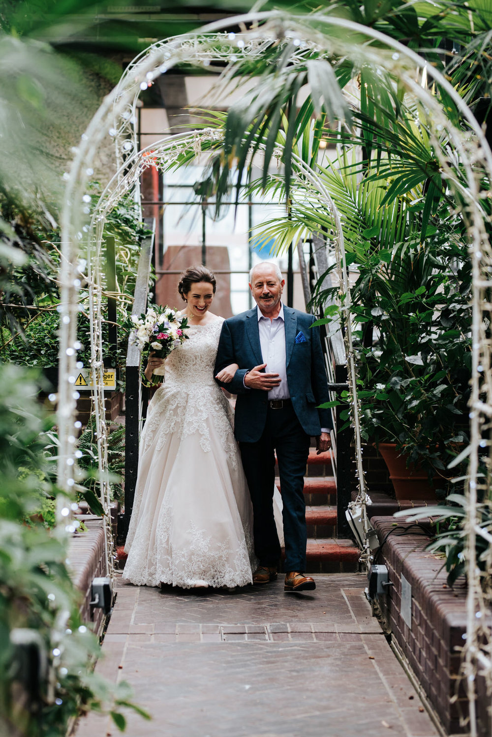 Bride and her uncle walk through lush greener and approach the a
