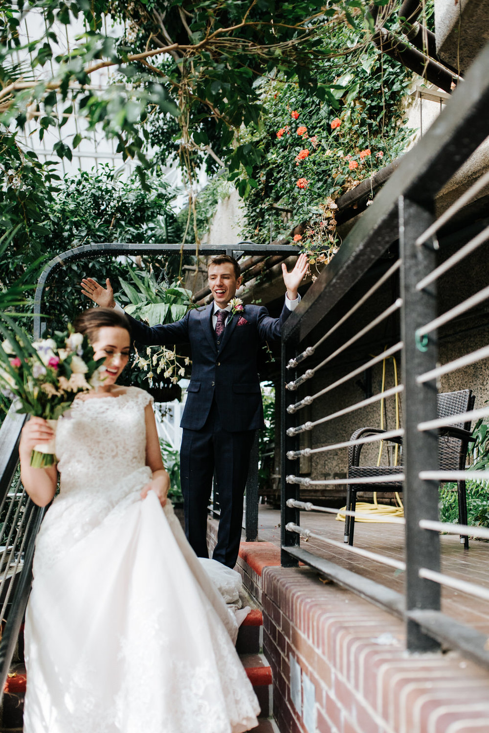 Bride walks down stairs in Barbican Centre as groom cheers from 