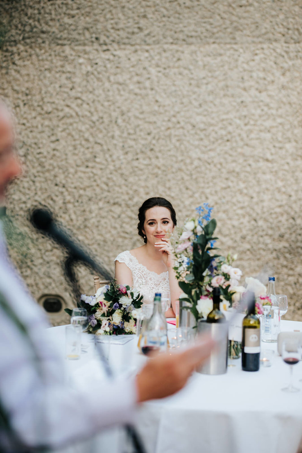  Bride looks emotional and grateful as close family member delivers a wedding speech 