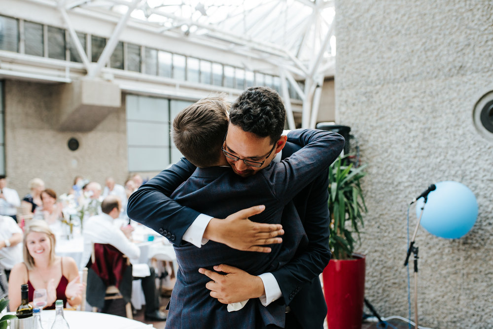 Best man hugs groom as guests smile from the back