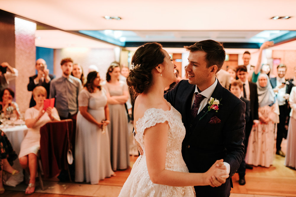 Bride and groom do their first dance as guests smile from behind