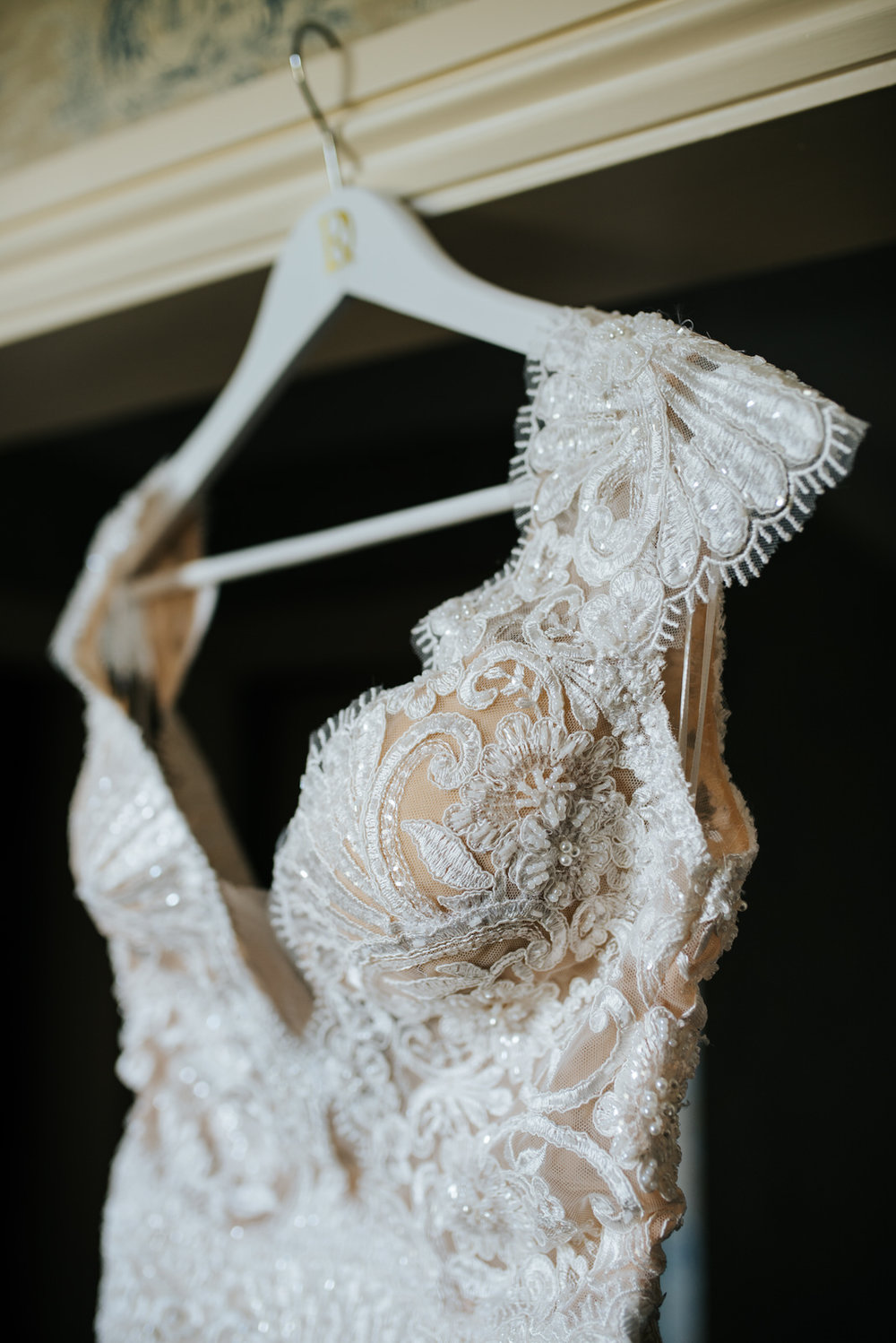 Bride's beautiful lace-detailed dress hangs on door