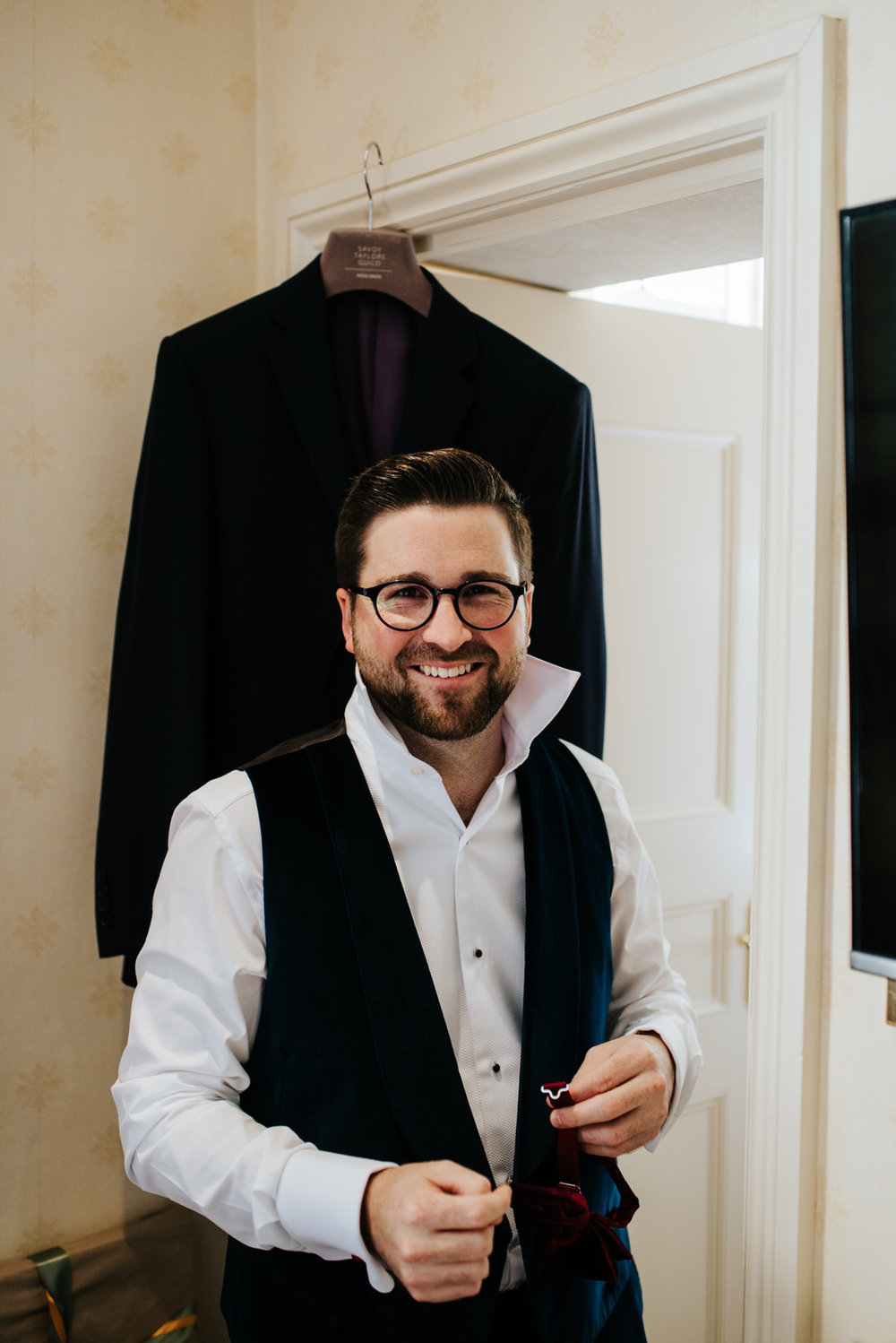 Groom smiles at camera as he buttons up his shirt