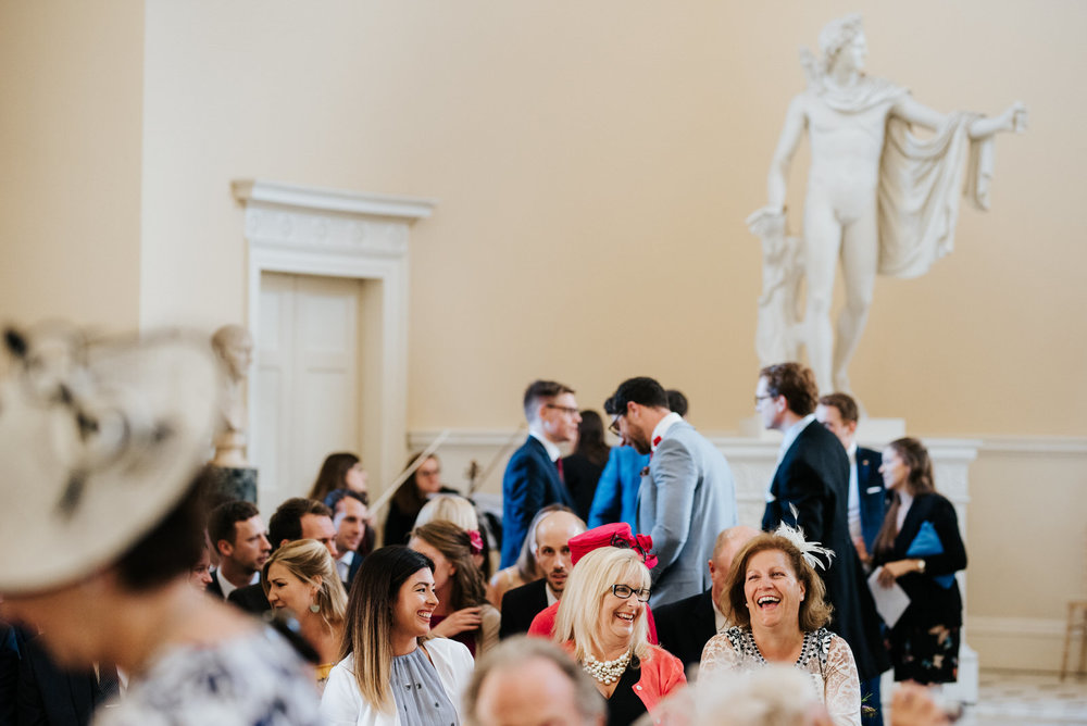 Guests smile and laugh as they wait for wedding ceremony to begin in Syon House