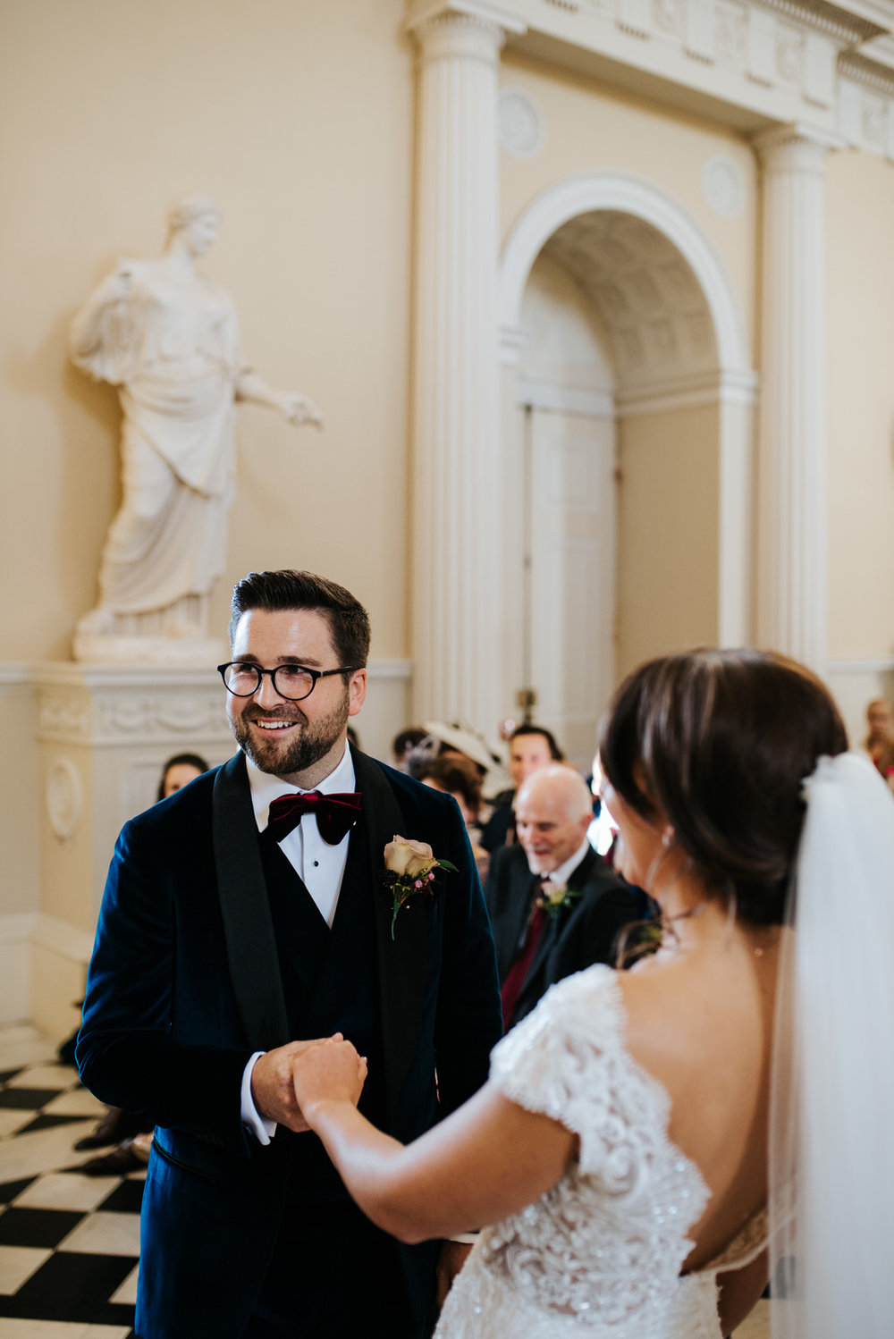 Groom smiles as he holds bride's hand while repeating wedding vows