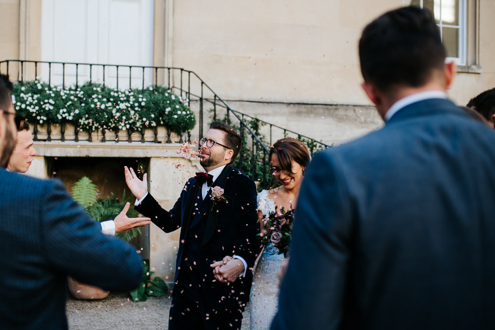 Guests throw confetti as couple walks in front of them 