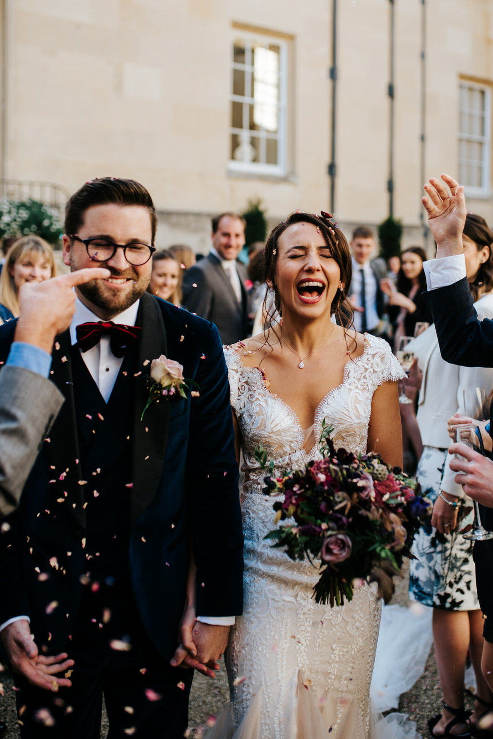 Bride and groom pull funny faces as confetti is thrown at them after wedding ceremony