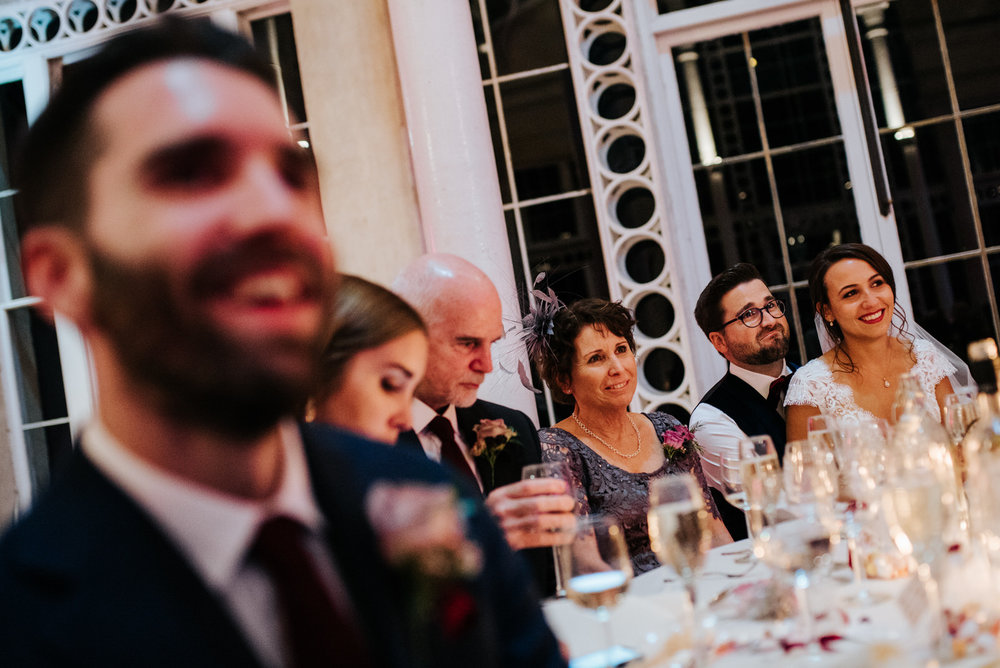 Photograph of bride, groom and family listening to wedding speeches