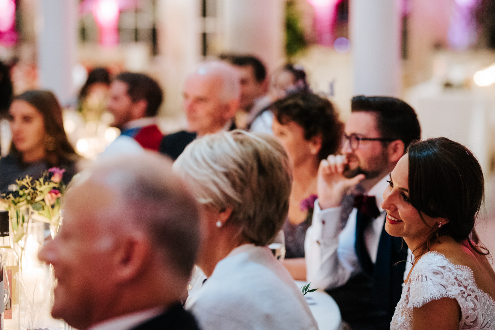 Bride and groom smile as they listen to groomsmen deliver emotional speech