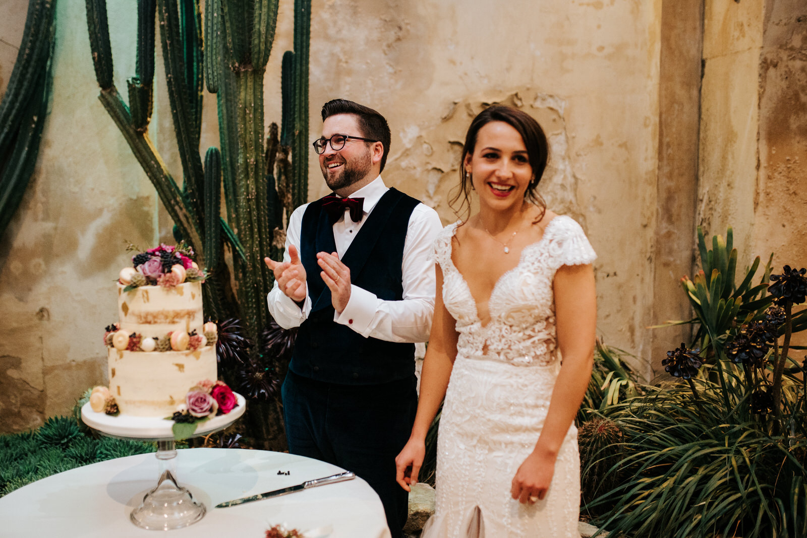 Bride and groom stand and smile moments before cutting their wedding cake