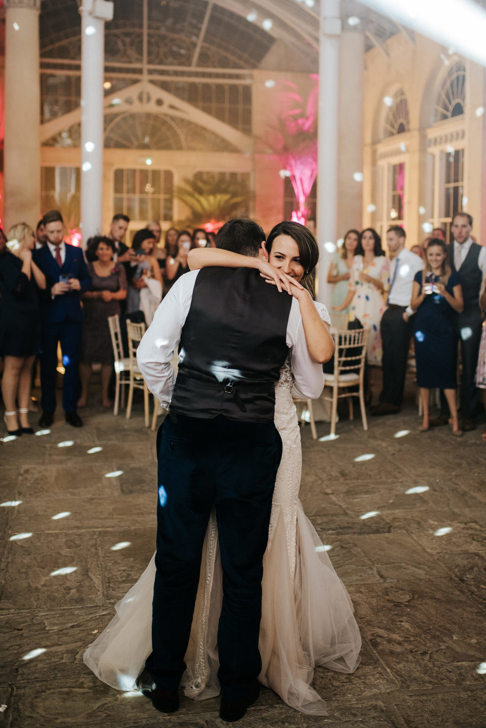 Bride hugs groom as they begin their first dance, flanked by guests