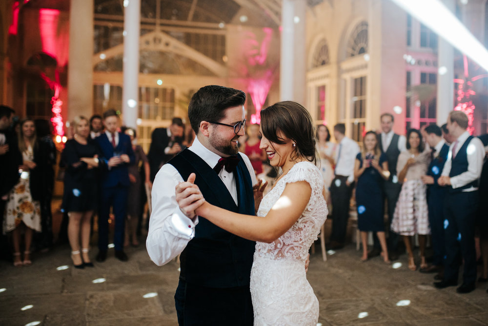 Bride and groom hold hands and dance during first dance as guests look from the back