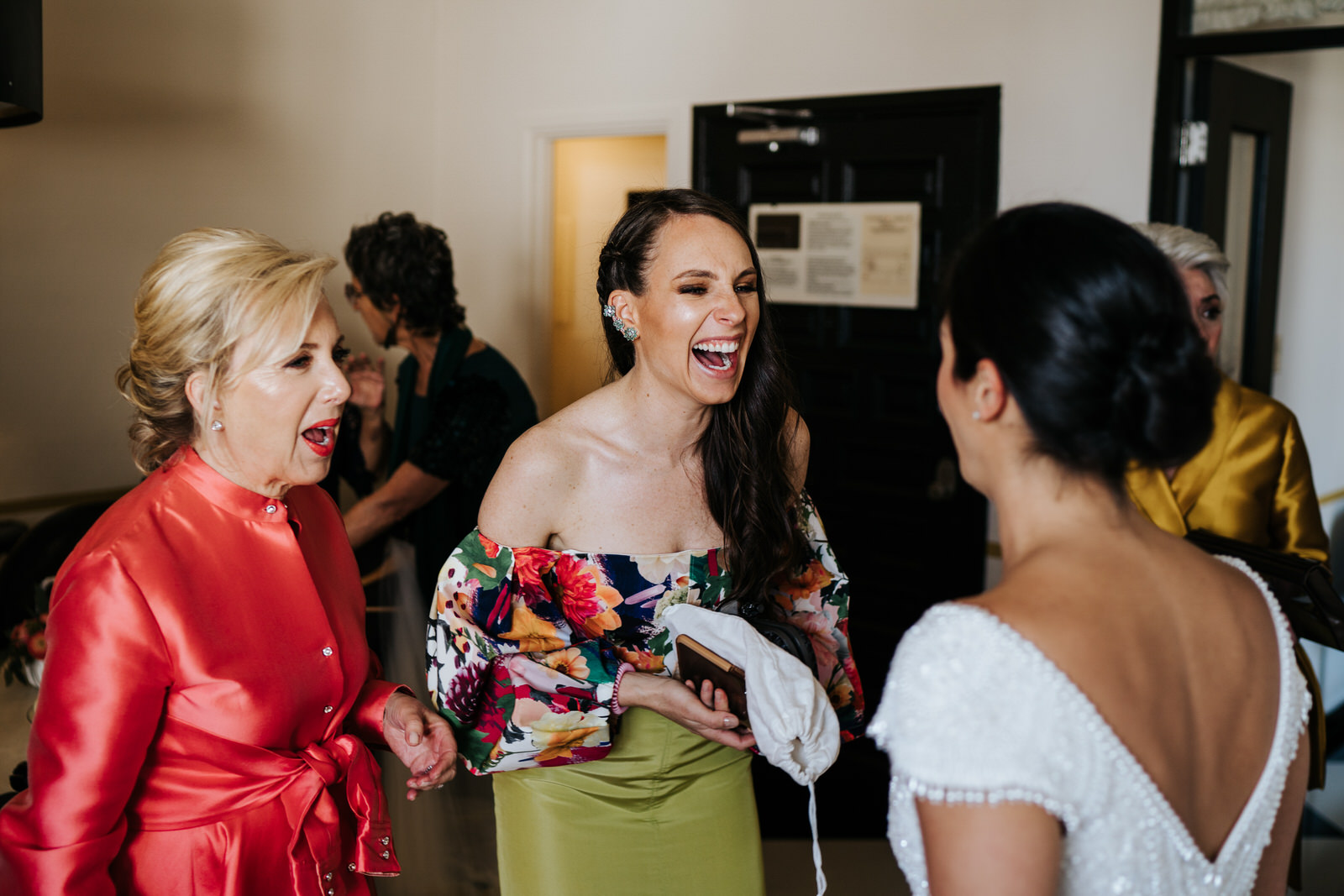 Groom's mom and other sister smile at bride in excitement and anticipation for the wedding celebrations ahead
