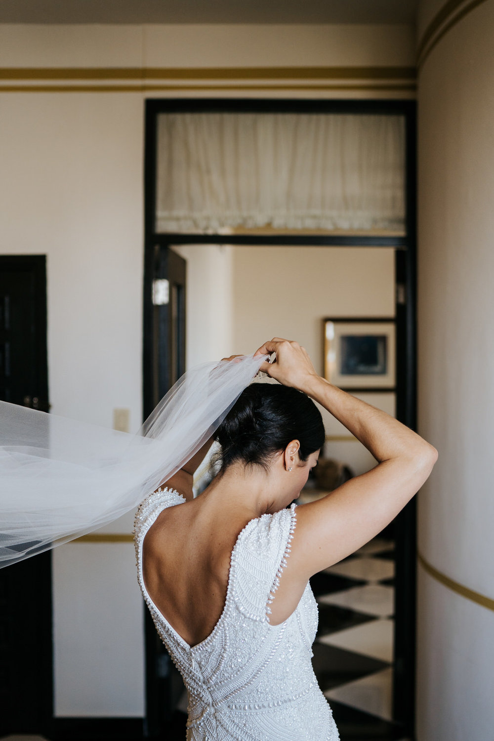  Bride, in her dress, puts on veil in hotel room 