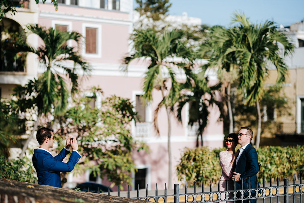  Guests take photos next to ceremony spot in Old San Juan while sun shines on the palm trees in the background 