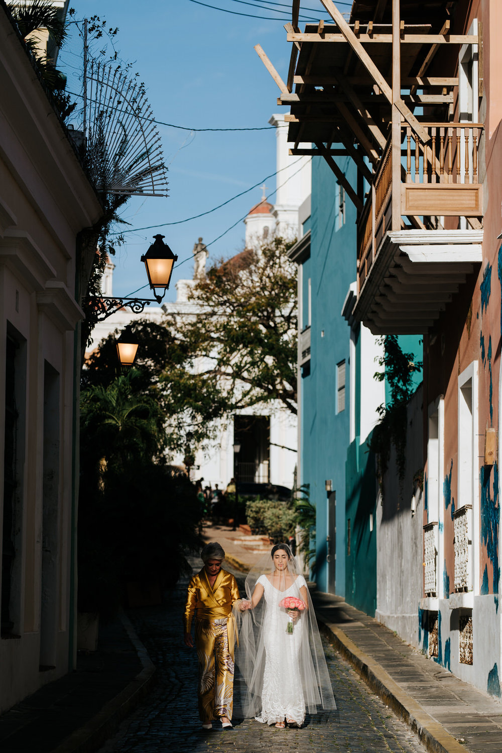  Bride and her mother walk down the streets of Old San Juan towards the wedding aisle as very dramatic lightning shines on them both 
