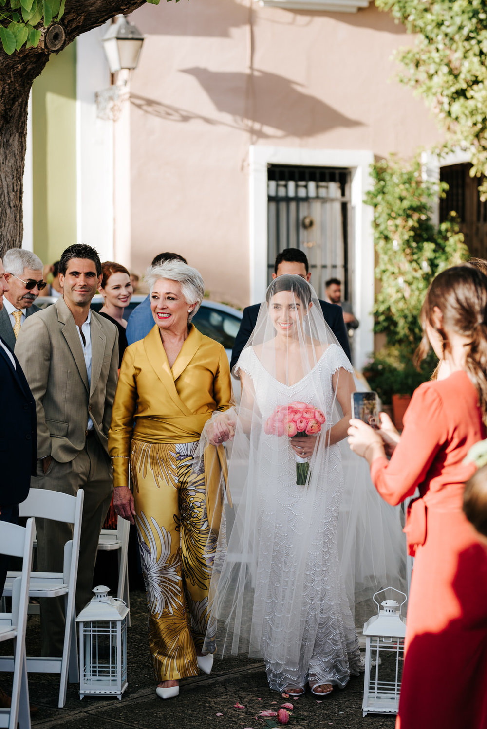  Bride and her mother walk down the wedding aisle as they smile and exchange glances with guests during this wedding in Old San Juan Puerto Rico 
