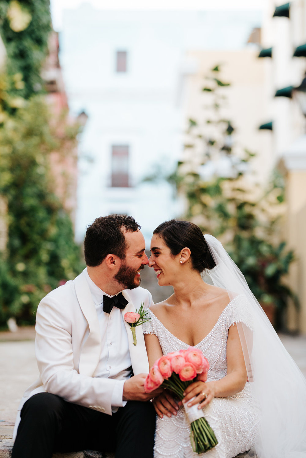  Close-up of bride and groom sitting on cobblestone steps in alley in Old San Juan while their noses touch 