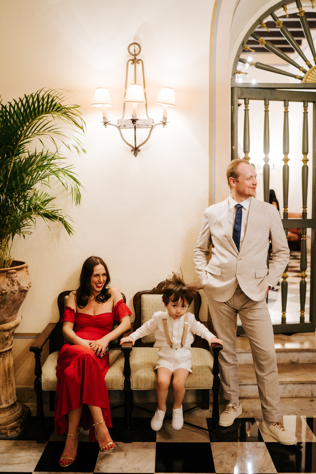 Bride's best friend, her husband and young son pose for a photo while parents smile and son jumps up and down in his chair