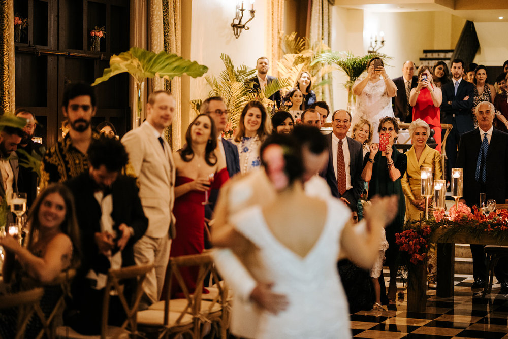  Bride and groom during their first dance, out of focus, while everyone in the background smiles at them and some guests take photos 