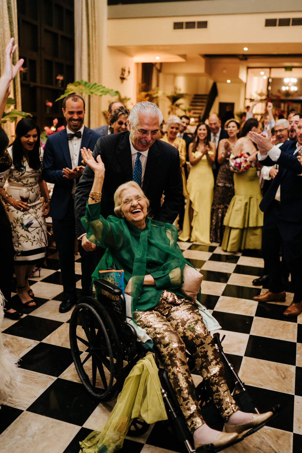  Bride's grandmother is on the dancefloor in her wheelchair and smiling as everyone encourages her and she waves 