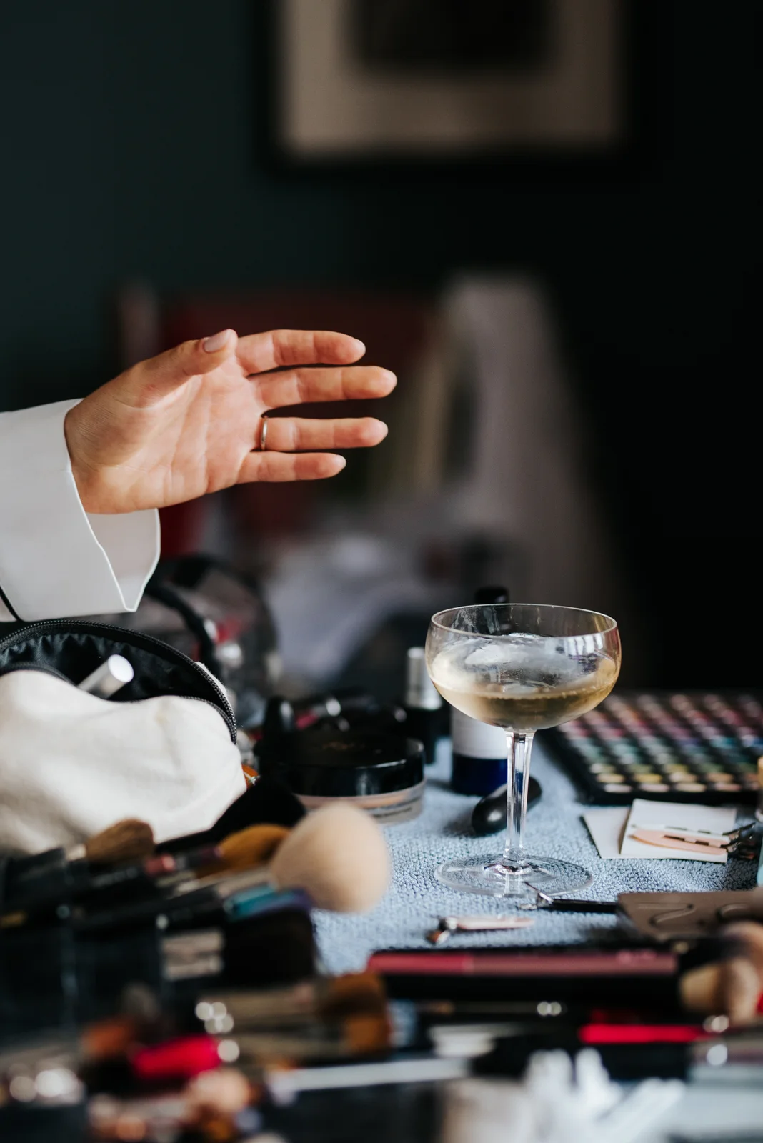 Bride reaches for glass of champagne which sits on makeup table