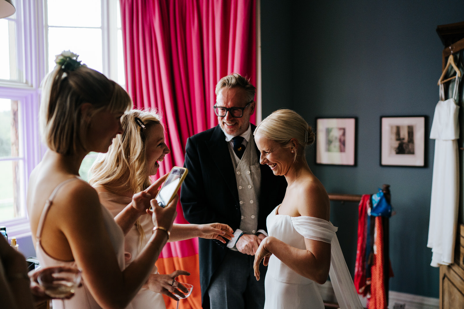 Bride, father of the bride, best friend of the bride and sister of the bride smile after seeing the bride in her dress