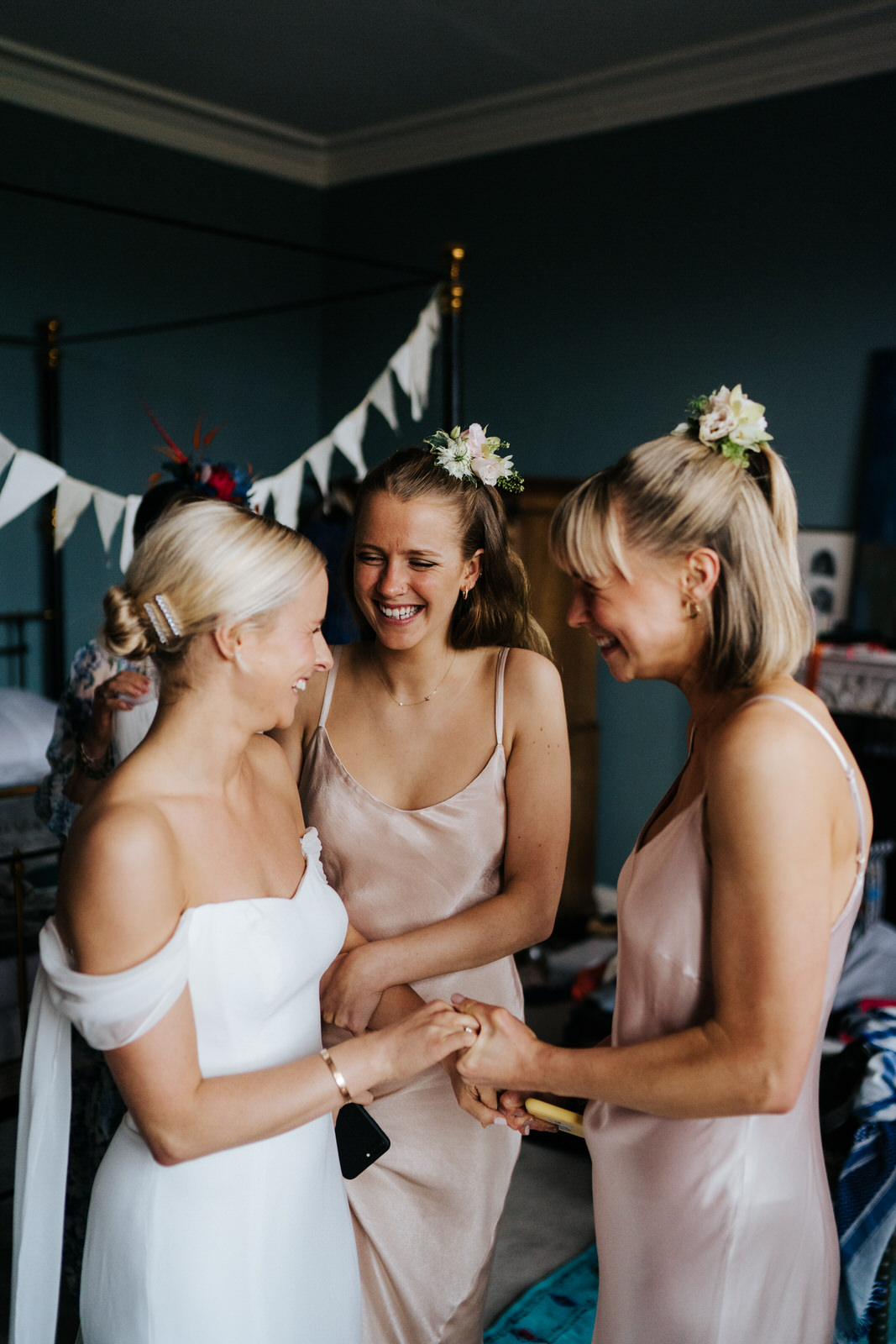  Bride holds hands and smiles at two sister in excited anticipation for the wedding ceremony 