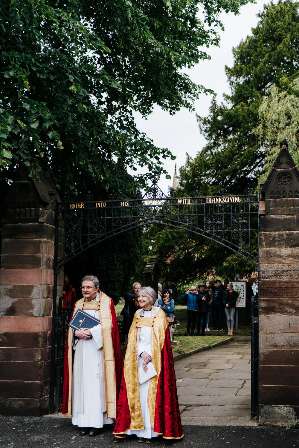  Vicars patiently await arrival of the bride outside of the village church in Hawarden, Wales 