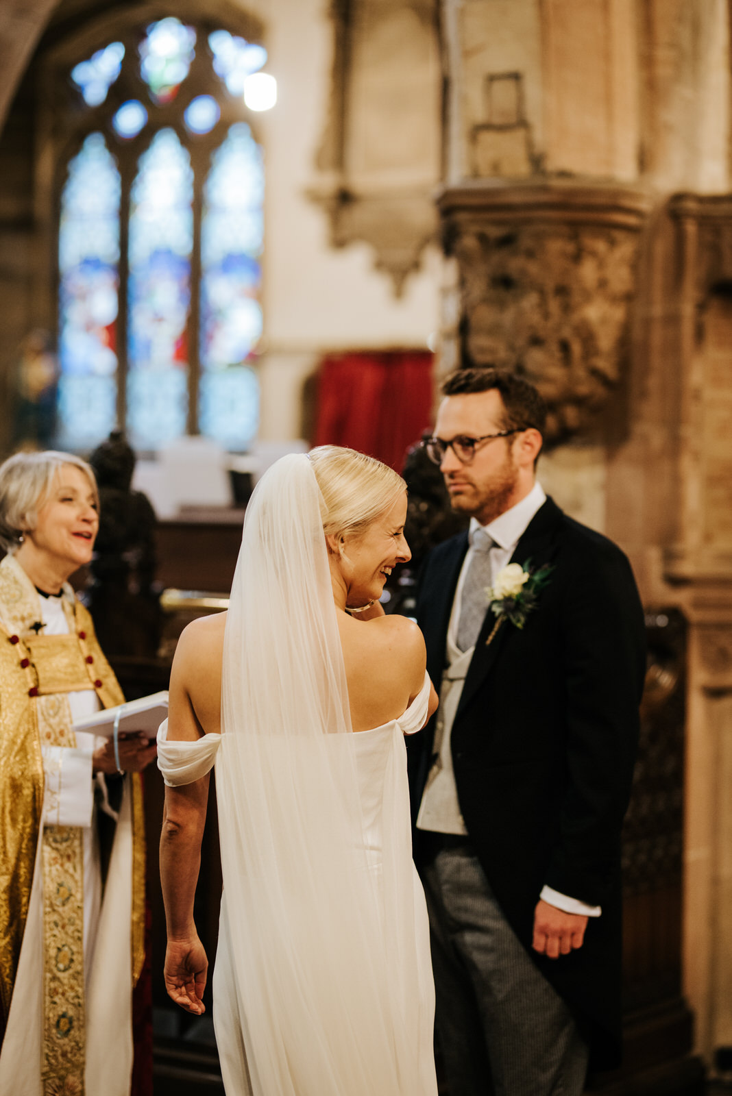  Bride and groom stand at the front of the church during ceremony, while bride looks back at family and smiles 5 