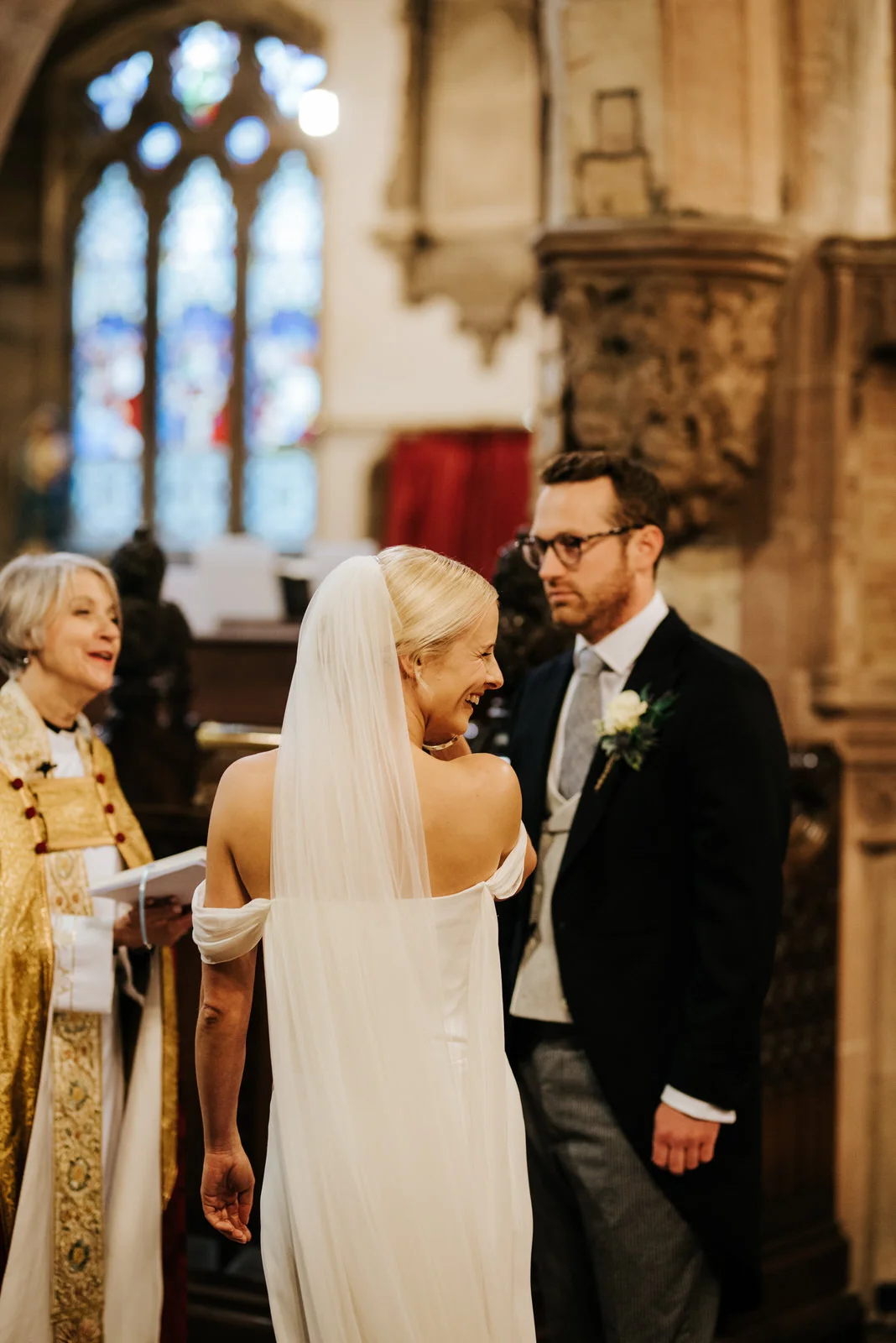 Bride and groom stand at the front of the church during ceremony, while bride looks back at family and smiles 5