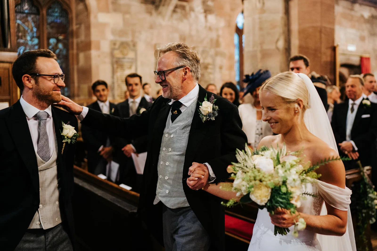 Bride and father of the bride arrive at the front of the aisle and hug the groom