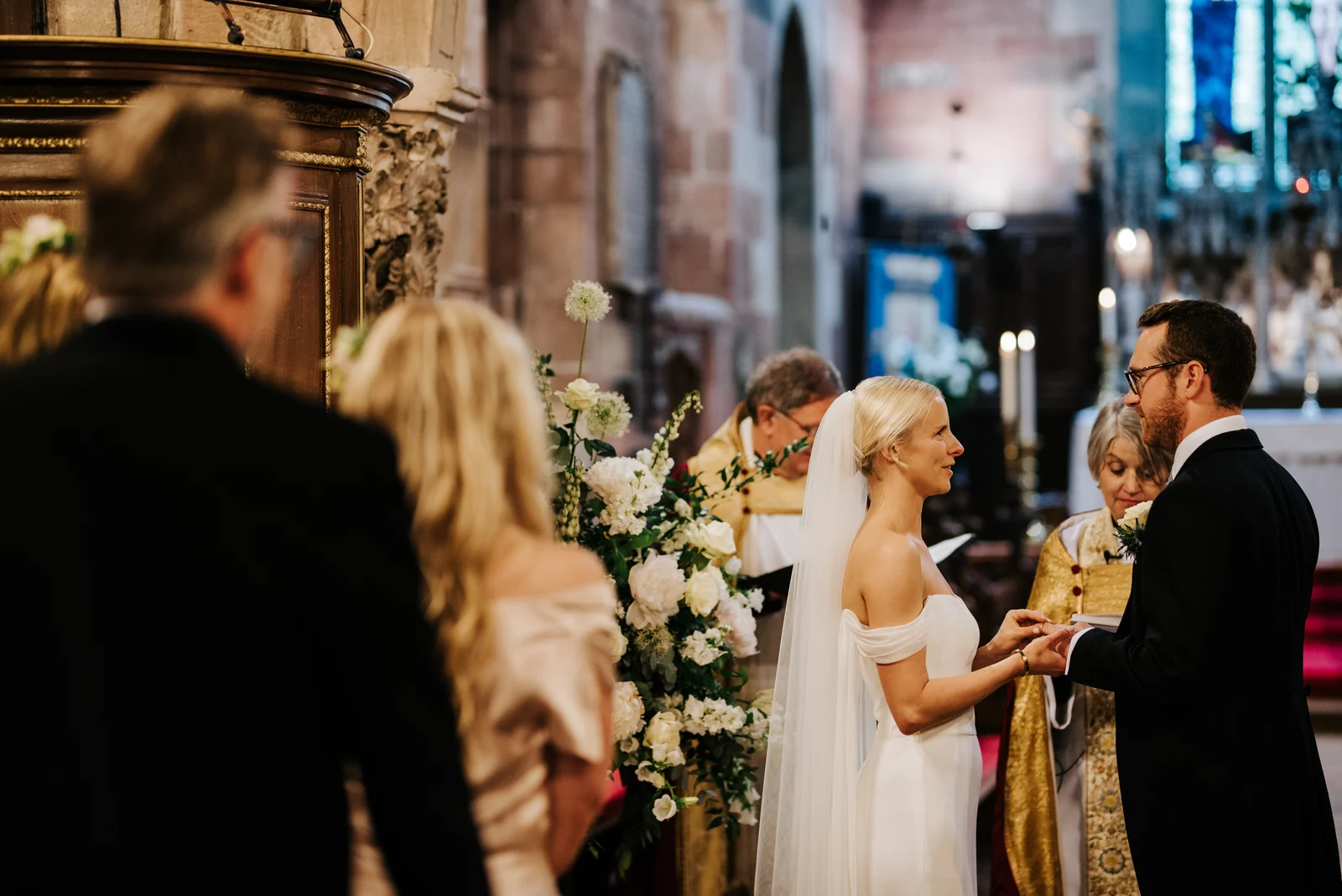 Bride and groom hold hands and exchange rings during wedding ceremony in Hawarden, Wales