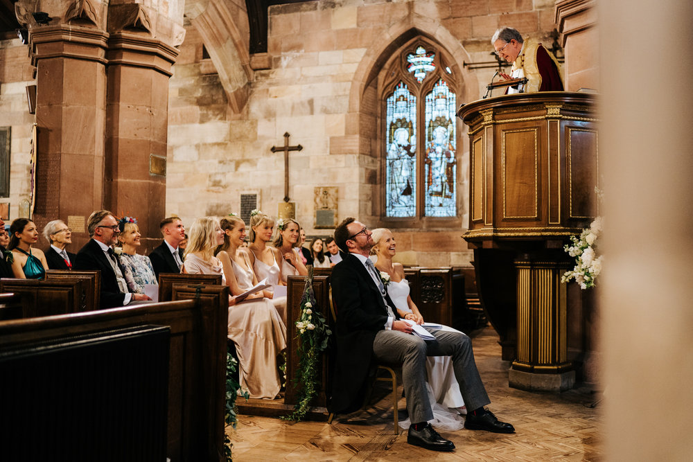  Bride and groom, and bride's family listen attentively to vicar's sermon and smile while doing so 