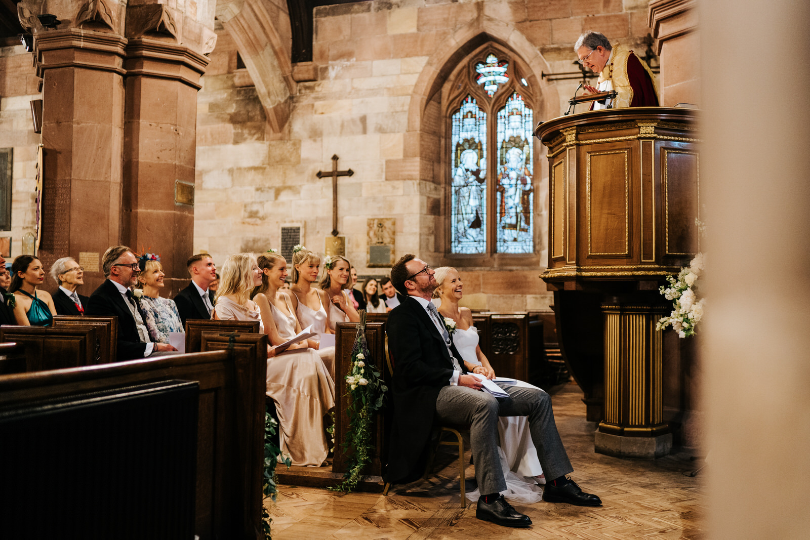 Bride and groom, and bride's family listen attentively to vicar's sermon and smile while doing so