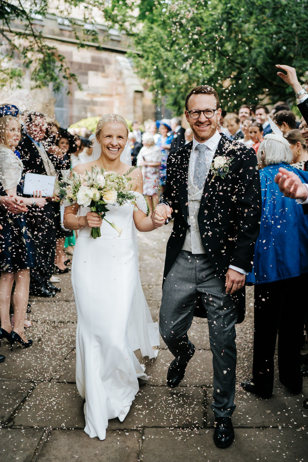  Bride and groom exit the church and walk down the pathway as guests throw confetti at them 