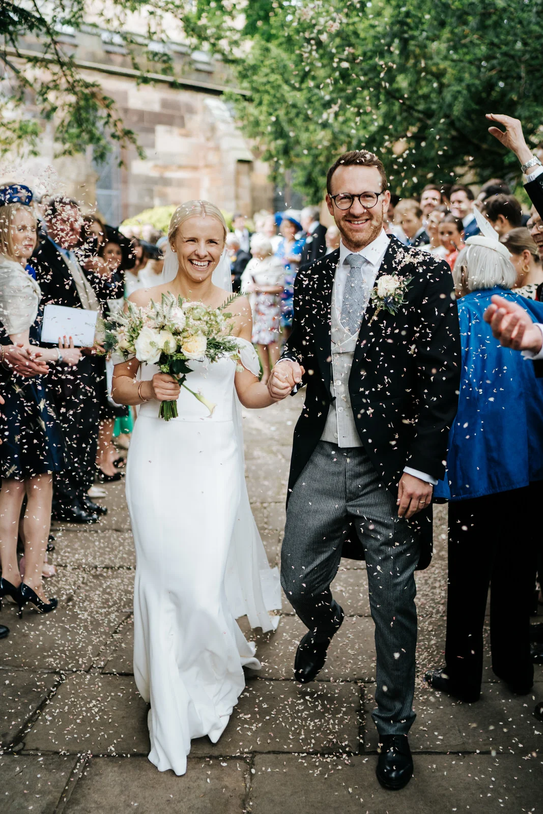 Bride and groom exit the church and walk down the pathway as guests throw confetti at them