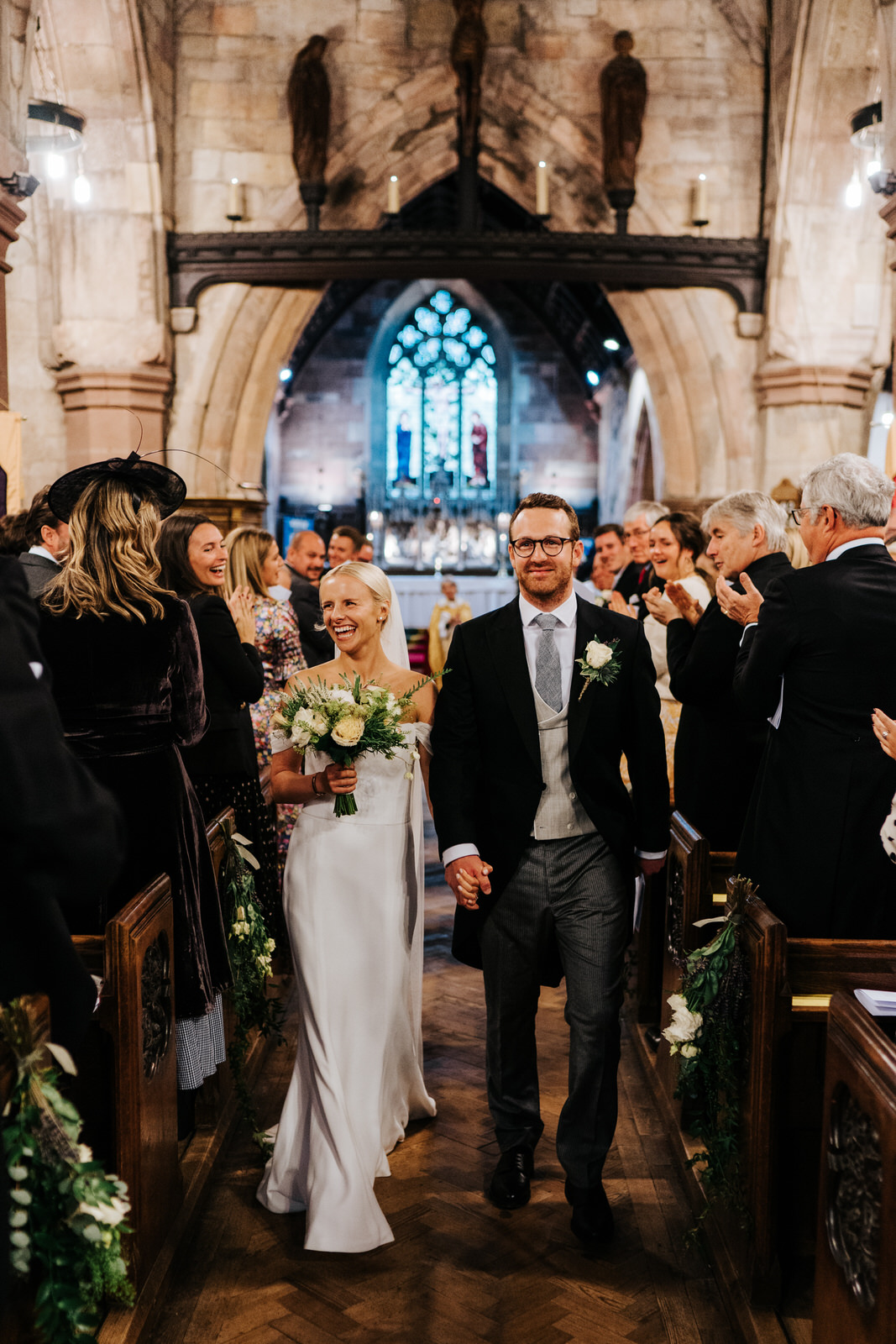  Bride and groom hold hands and walk back down the aisle as husband and wife while smiling at their guests ] 