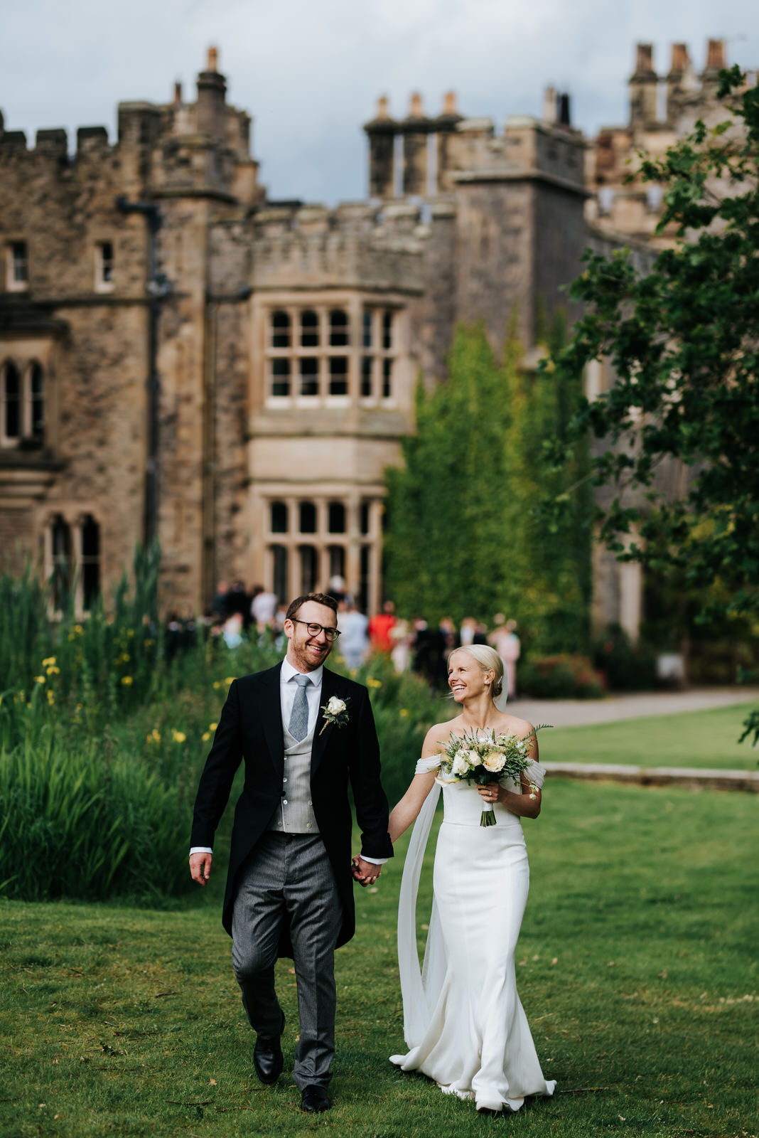 Bride and groom walk towards camera with Hawarden Castle in the background