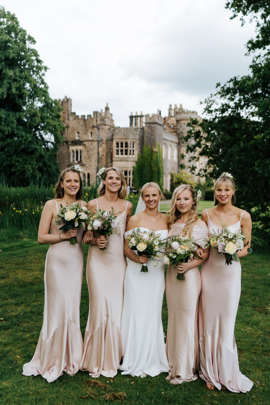 Posed photograph of bridesmaids and bride holding bouquets with Hawarden Castle in the background
