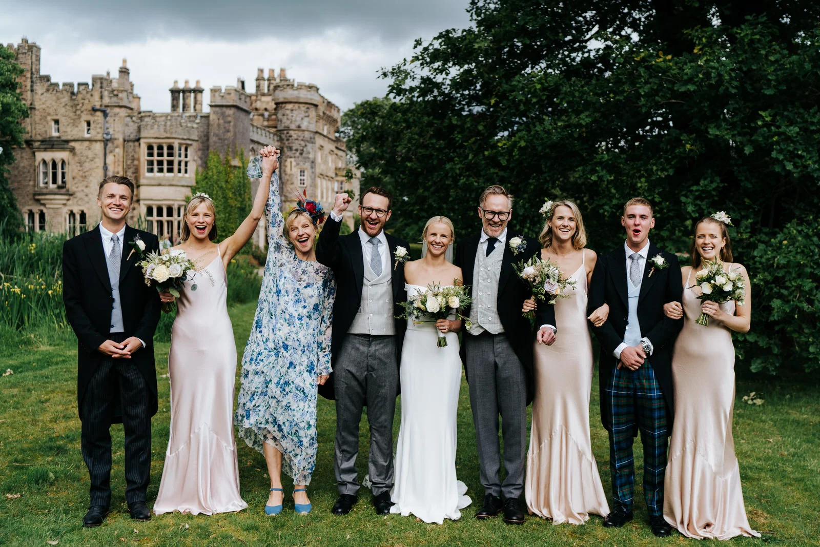 Posed family photograph of bride, groom and bride's family with Hawarden Castle in the background
