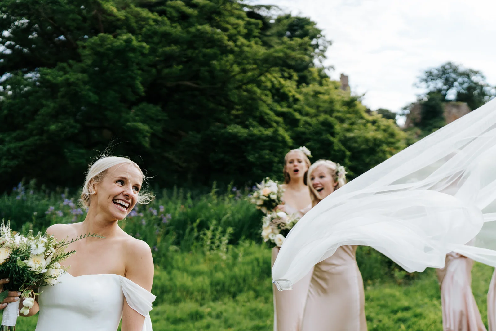 Bride's veil flies out of her hair as bridesmaids look on in amazement